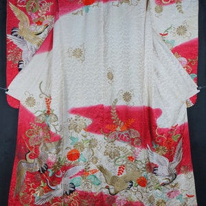 May include: A traditional Japanese kimono with a white background and red accents. The kimono is decorated with embroidered cranes and floral patterns in gold, green, and pink.