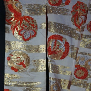 May include: A white kimono with gold and red embroidery. The kimono features a repeating pattern of stylized flowers and birds. The fabric is a silk blend.