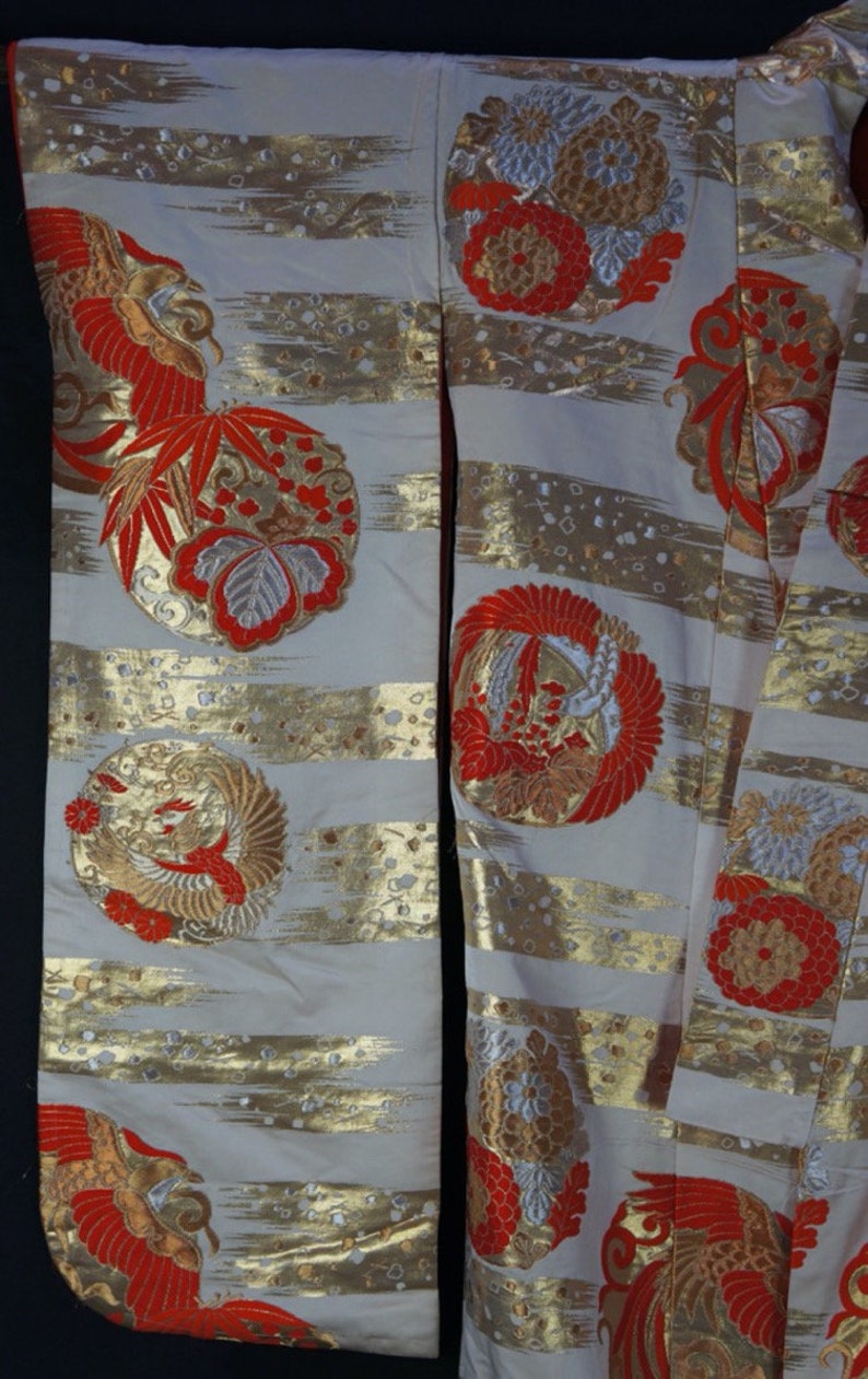 May include: A white kimono with gold and red embroidery. The kimono features a repeating pattern of stylized flowers and birds. The fabric is a silk blend.