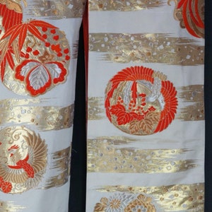 May include: A white kimono with gold and red embroidery. The embroidery features a variety of floral and bird designs. The kimono is made of a soft, silky fabric.