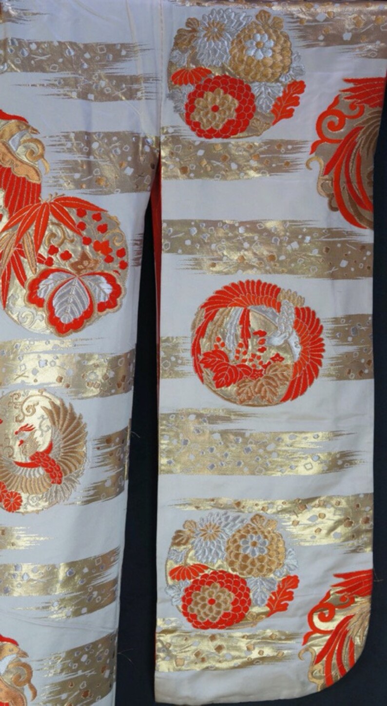 May include: A white kimono with gold and red embroidery. The embroidery features a variety of floral and bird designs. The kimono is made of a soft, silky fabric.