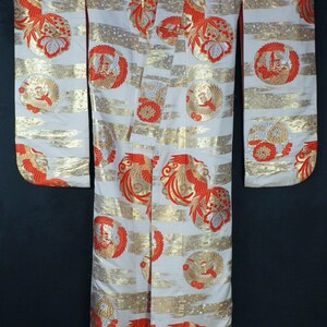 May include: A white kimono with a red and gold phoenix pattern. The kimono has a red trim and is made of a silky fabric.
