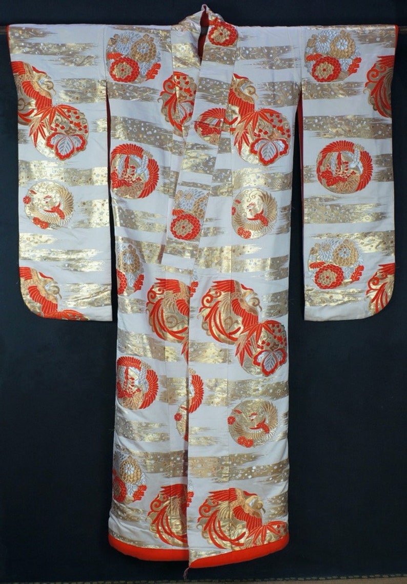 May include: A white kimono with a red and gold phoenix pattern. The kimono has a red trim and is made of a silky fabric.