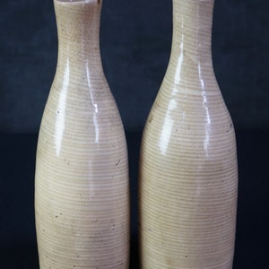 May include: Two off-white ceramic sake bottles with a ribbed texture. The bottles are similar in shape and size.