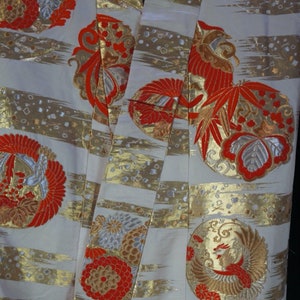 May include: A white kimono with gold and red embroidery. The kimono features a repeating pattern of stylized birds and flowers.