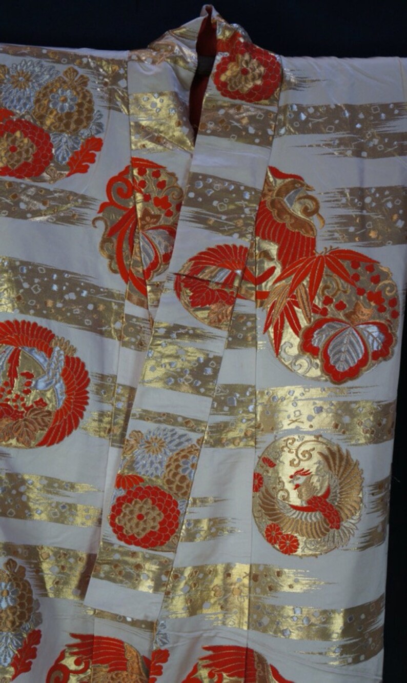 May include: A white kimono with gold and red embroidery. The kimono features a repeating pattern of stylized birds and flowers.