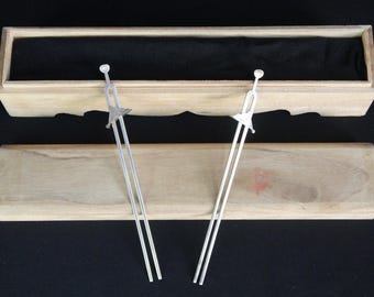 May include: Two silver-toned metal hair sticks with a sword-like design, featuring a long two-pronged shaft and a crossguard detail. The hair accessories are displayed with a light-colored wooden storage box that has a black interior lining.