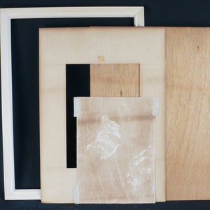 Puede incluir: Un marco blanco rodea una cartulina beige con una cartulina beige m&aacute;s peque&ntilde;a en el interior. Un trozo de papel con una mancha marr&oacute;n est&aacute; dentro de la cartulina m&aacute;s peque&ntilde;a.
