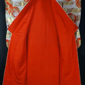 May include: A traditional Japanese kimono with a white and gold patterned exterior and a bright red interior. The kimono is open and laid flat, revealing the lining.