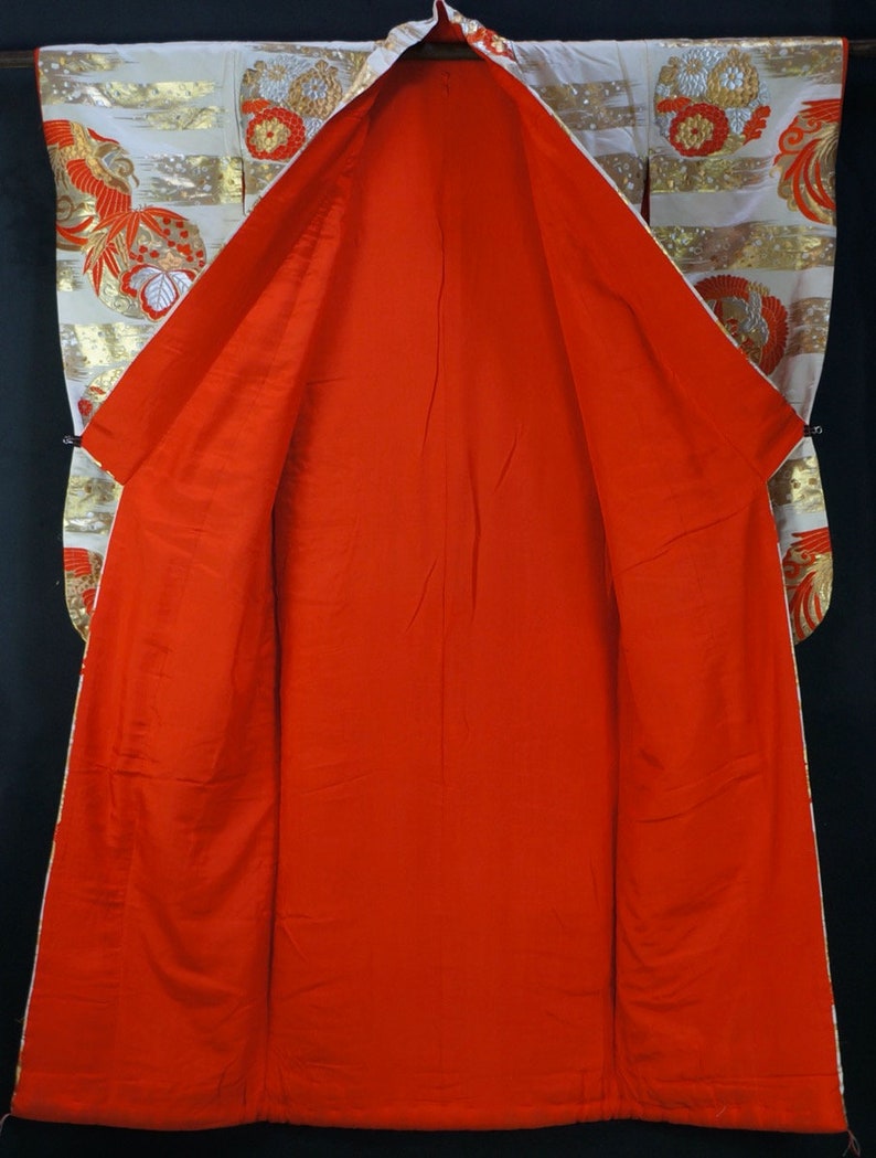 May include: A traditional Japanese kimono with a white and gold patterned exterior and a bright red interior. The kimono is open and laid flat, revealing the lining.
