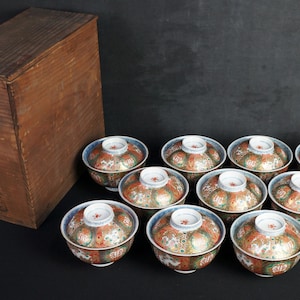Könnte beinhalten: Ein Set aus zehn kleinen, runden Porzellanschalen mit aufwendigen floralen und geometrischen Mustern in Blau-, Rot- und Goldtönen. Die Schalen sind in einem Kreis auf einer dunklen Oberfläche angeordnet.