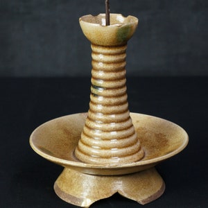 May include: A brown ceramic candlestick with a wide base and a tall, ribbed column. The candlestick has a small metal spike on top for holding a candle.