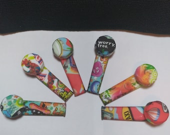 May include: Seven colorful silicone smoking pipes with various cartoon and graphic designs. The pipes are arranged in a semi-circle on a white surface.