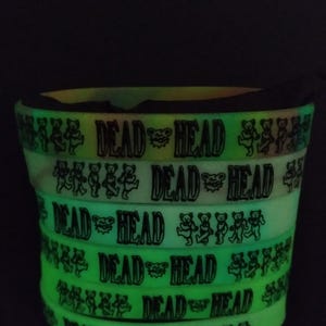 May include: A stack of glow-in-the-dark silicone bracelets with the words "Dead Head" and a dancing bear graphic printed on them.