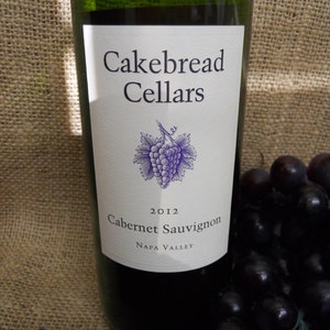May include: A green glass bottle of Cakebread Cellars 2012 Cabernet Sauvignon wine from Napa Valley. The label features a purple grape cluster and the winery's name.
