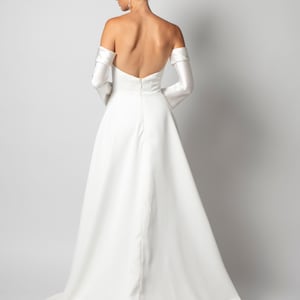 May include: A white off-the-shoulder wedding dress with a long train and bell sleeves. The dress has a fitted bodice and a flowing skirt.