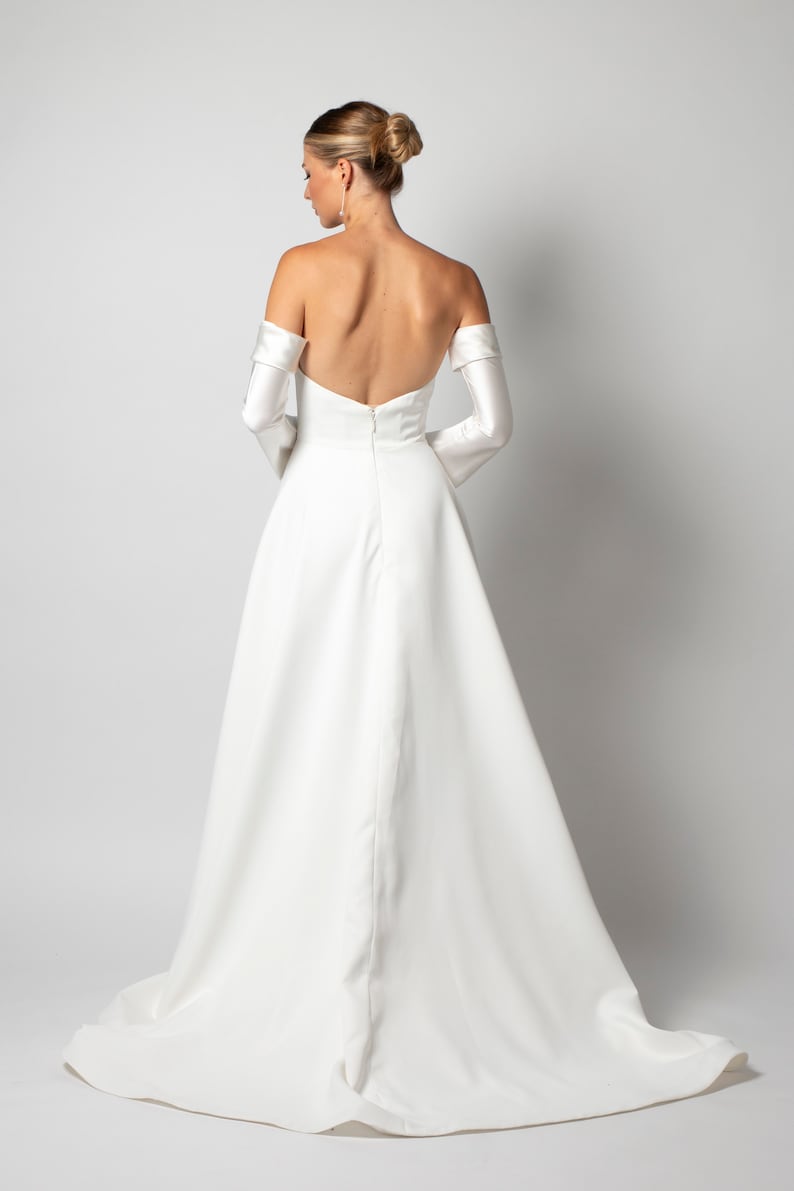 May include: A white off-the-shoulder wedding dress with a long train and bell sleeves. The dress has a fitted bodice and a flowing skirt.