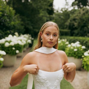 May include: A white strapless wedding dress with a beaded bodice and a flowing skirt. The dress is being held up by the wearer's hands.