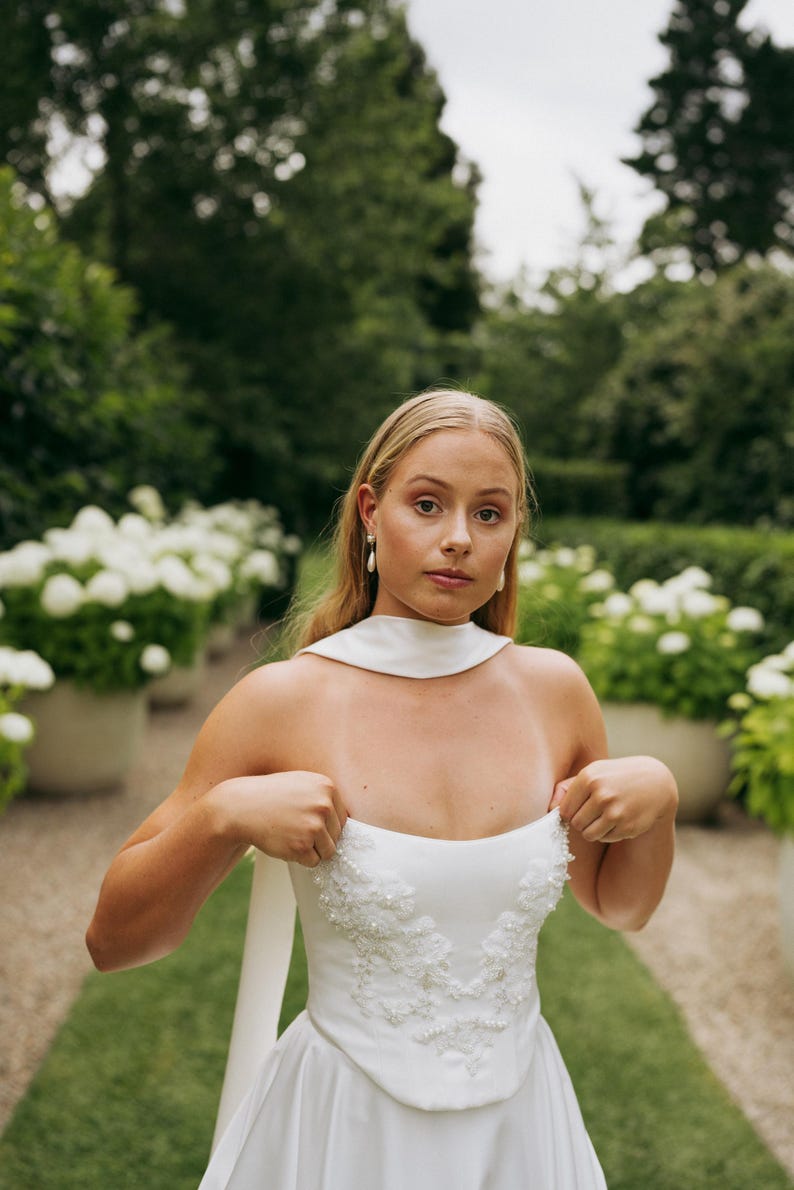 May include: A white strapless wedding dress with a beaded bodice and a flowing skirt. The dress is being held up by the wearer's hands.