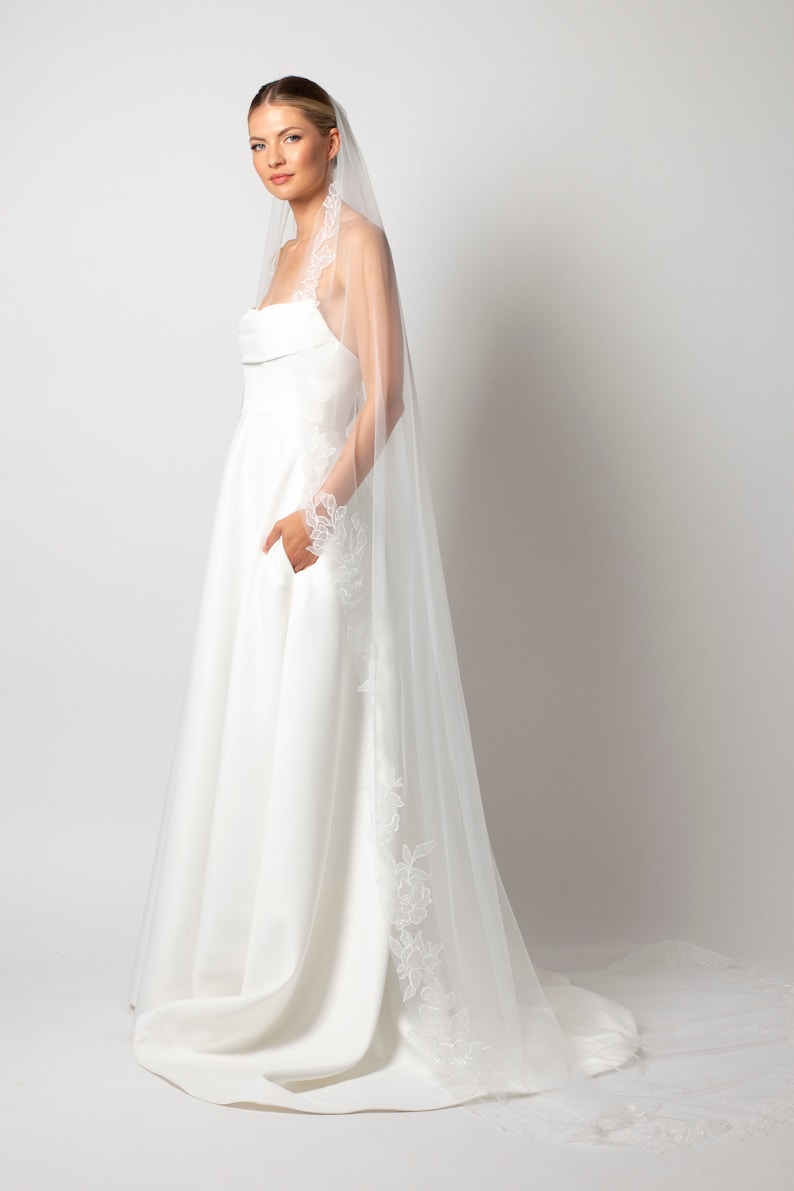 May include: A white wedding dress with a lace trim and a long white veil