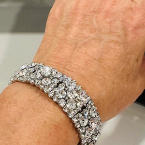 Puede incluir: Un brazalete plateado con múltiples filas de brillantes transparentes.