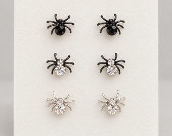 May include: Three pairs of spider-shaped stud earrings arranged in a vertical column. The top pair is black with black crystals, the middle pair is black with clear crystals, and the bottom pair is silver-toned metal with clear crystals.
