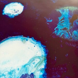 May include: Abstract painting with swirling blue, white, and green paint on a dark purple background.