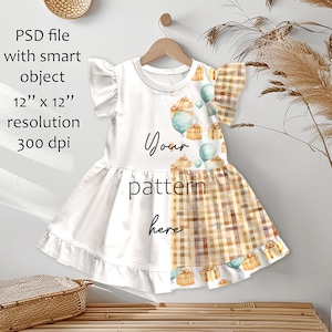 May include: A white and patterned dress with a round neckline and short sleeves. The dress features a design of balloons and gift boxes. The text "Your pattern here" is visible on the dress. The dress is hanging on a wooden hanger.