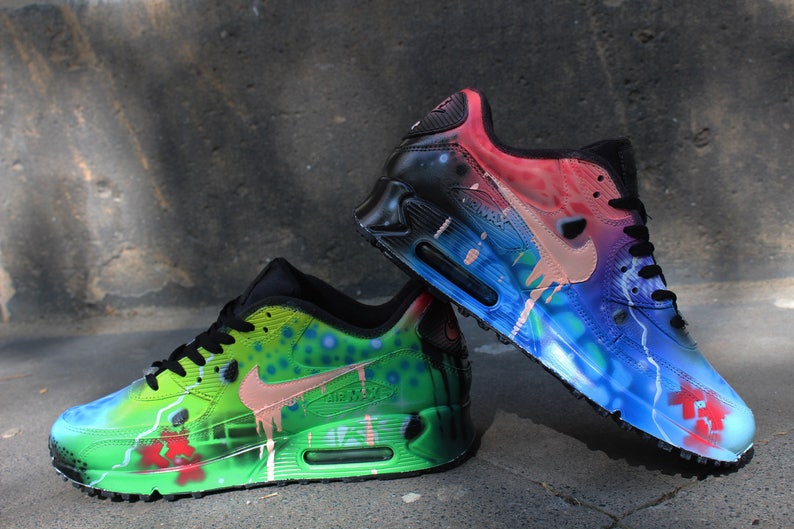 Puede incluir: Un par de zapatillas Nike Air Max 90 pintadas a mano. Una zapatilla est&aacute; pintada en tonos de verde, azul y rosa, mientras que la otra est&aacute; pintada en tonos de azul, rosa y negro. Ambas zapatillas presentan un dise&ntilde;o &uacute;nico de pintura salpicada.