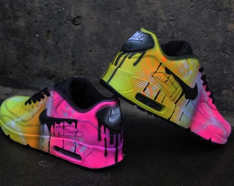 Könnte beinhalten: Ein Paar individuell bemalte Nike Air Max 90 Sneaker. Ein Schuh ist gelb, pink und schwarz mit einem Tropfeffekt. Der andere Schuh ist pink, gelb und schwarz mit einem Tropfeffekt.