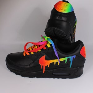 Puede incluir: Zapatillas Nike Air Max 90 de cuero negro con un dise&ntilde;o de goteo de arco&iacute;ris en el swoosh y el panel lateral. Los cordones son de arco&iacute;ris.