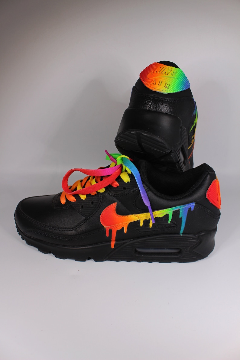 Puede incluir: Zapatillas Nike Air Max 90 de cuero negro con un dise&ntilde;o de goteo de arco&iacute;ris en el swoosh y el panel lateral. Los cordones son de arco&iacute;ris.