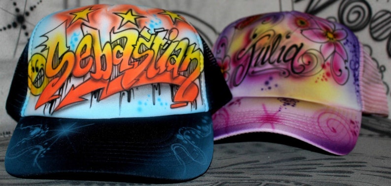 Peut inclure: Deux casquettes de camionneur personnalis&eacute;es. L'une est noire avec un filet blanc &agrave; l'arri&egrave;re et porte le nom "Sebastian" en lettres de style graffiti color&eacute;es. L'autre est rose avec un filet blanc &agrave; l'arri&egrave;re et porte le nom "Julia" en &eacute;criture cursive avec des motifs floraux.