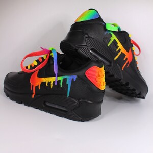 Puede incluir: Zapatillas Nike Air Max 90 negras con pintura de arco&iacute;ris goteando por los lados. Los cordones est&aacute;n atados con un esquema de colores de arco&iacute;ris.