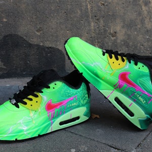 Puede incluir: Un par de zapatillas Nike Air Max verdes y negras con detalles en rosa y amarillo. Las zapatillas tienen un dise&ntilde;o de rayo y un efecto de pintura que gotea.