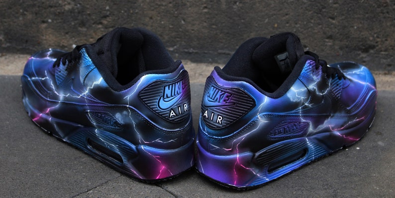 May include: A pair of black Nike Air Max 90 sneakers with a custom lightning bolt design in shades of blue, purple, and pink.