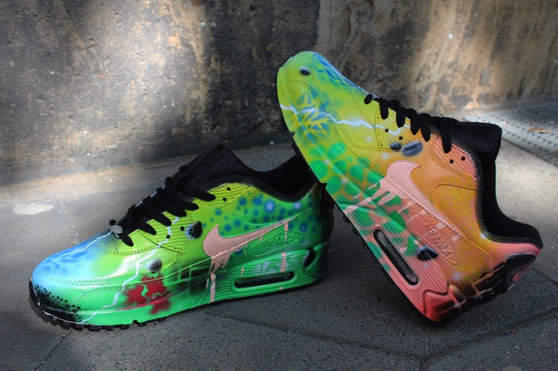 Puede incluir: Un par de zapatillas Nike Air Max 90 pintadas a mano. Las zapatillas est&aacute;n pintadas en un esquema de colores verde, azul y naranja vibrantes con una variedad de dise&ntilde;os abstractos. Las zapatillas tienen cordones negros y un logotipo swoosh negro.