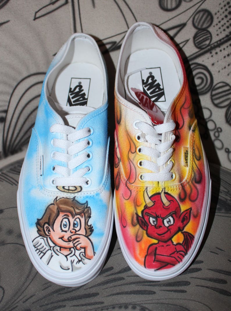 K&ouml;nnte beinhalten: Ein Paar ma&szlig;gefertigte Vans-Sneaker mit handgemalten Designs. Ein Schuh zeigt einen blauen Himmel mit einem Comic-Engel, w&auml;hrend der andere Schuh einen roten Teufel mit Flammen hat.