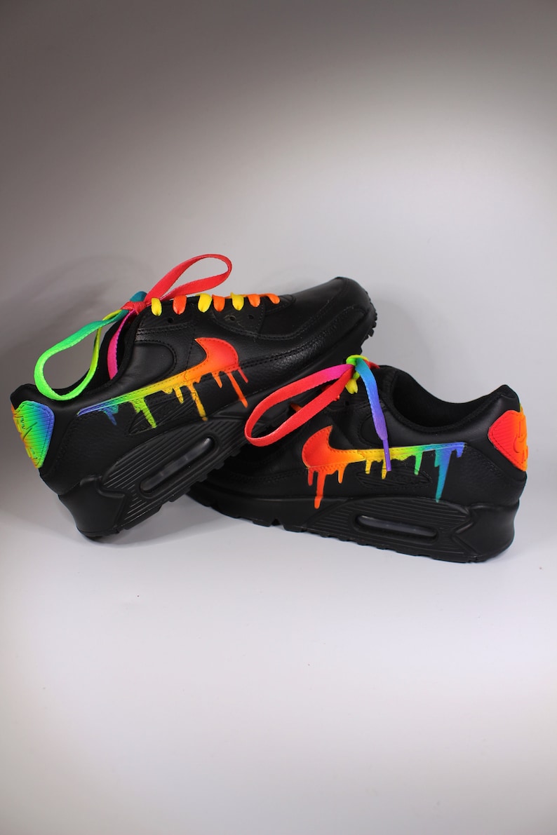 Puede incluir: Un par de zapatillas Nike Air Max 90 negras con pintura de goteo arco&iacute;ris y cordones de colores.