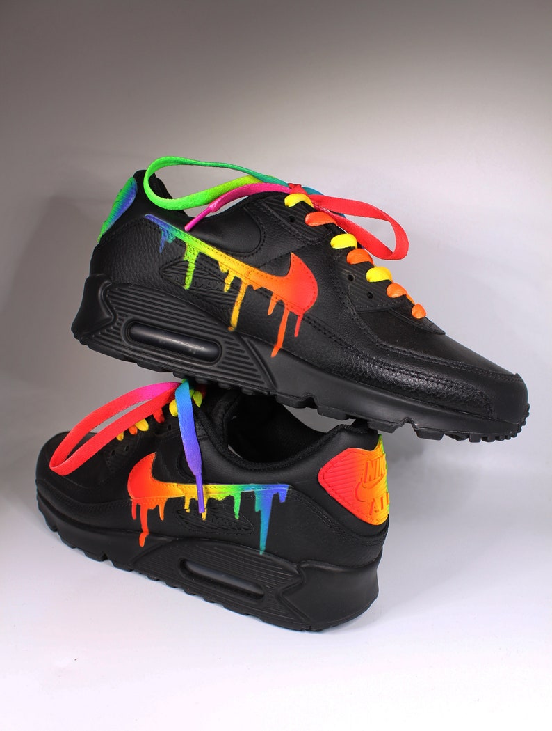 Puede incluir: Zapatillas Nike Air Max 90 negras con un dise&ntilde;o de pintura de goteo arco&iacute;ris. Las zapatillas tienen cordones amarillos y un logotipo swoosh negro.