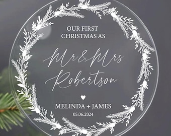 May include: A clear round Christmas ornament with a white wreath design. The ornament says "Our First Christmas as Mr & Mrs Robertson Melinda + James 05.06.2024".
