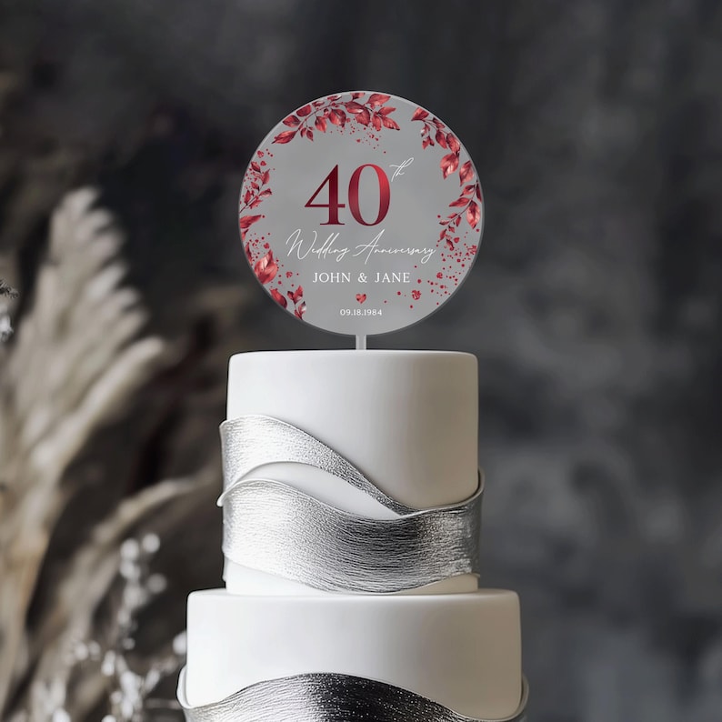 May include: A round cake topper with a grey background and red floral accents. The topper features the number 40 in red, the text "Wedding Anniversary", and the names "John & Jane" with the date "05.18.1984".