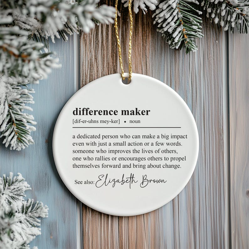 May include: White ceramic bauble with the definition of "difference maker" and the name "Elizabeth Brown" printed in black.