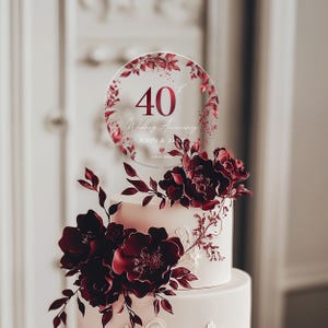 May include: A clear acrylic cake topper with a burgundy floral design and the text "40th Wedding Anniversary John & Jane 09.18.1983".