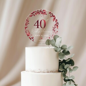 May include: A round, clear acrylic cake topper with a red floral design. The topper features the number 40, the words "Wedding Anniversary", the names "JOHN & JANE", and the date "09.18.1984".