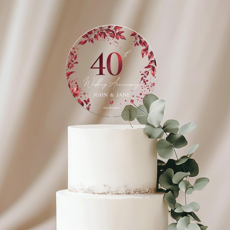 May include: A round, clear acrylic cake topper with a red floral design. The topper features the number 40, the words "Wedding Anniversary", the names "JOHN & JANE", and the date "09.18.1984".
