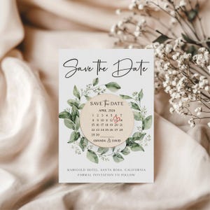 Puede incluir: Tarjeta de guardar la fecha con un dise&ntilde;o floral verde de hojas. La tarjeta presenta un c&iacute;rculo de madera con un calendario que muestra abril de 2024 con un coraz&oacute;n rojo marcando el 13. El texto dice "Save the Date", "Abril 2024", "Amanda & David", "Marigold Hotel, Santa Rosa, California", y "Invitaci&oacute;n formal a seguir".