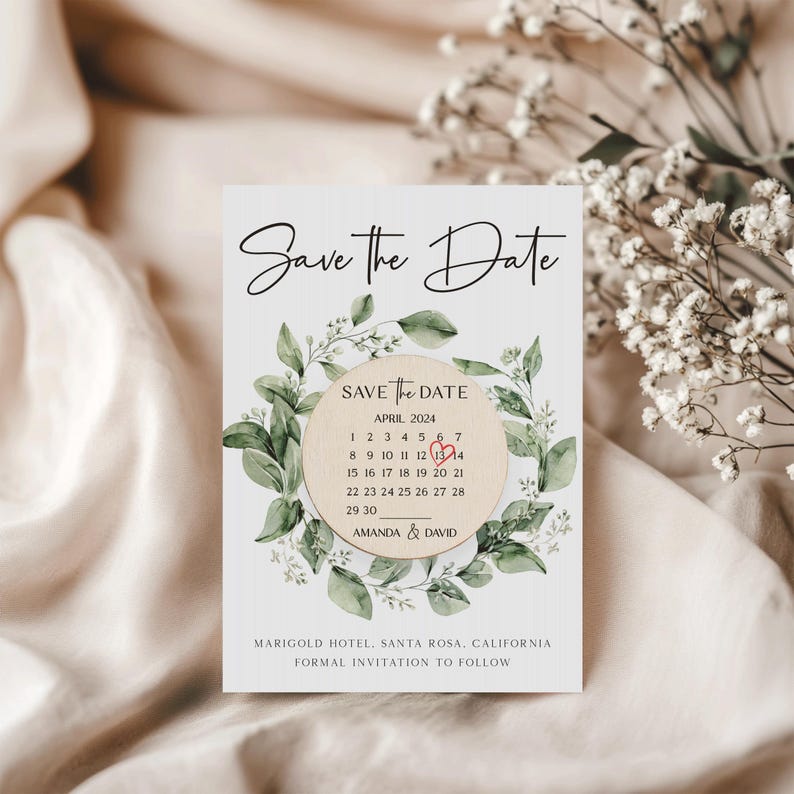 Puede incluir: Tarjeta de guardar la fecha con un dise&ntilde;o floral verde de hojas. La tarjeta presenta un c&iacute;rculo de madera con un calendario que muestra abril de 2024 con un coraz&oacute;n rojo marcando el 13. El texto dice "Save the Date", "Abril 2024", "Amanda & David", "Marigold Hotel, Santa Rosa, California", y "Invitaci&oacute;n formal a seguir".