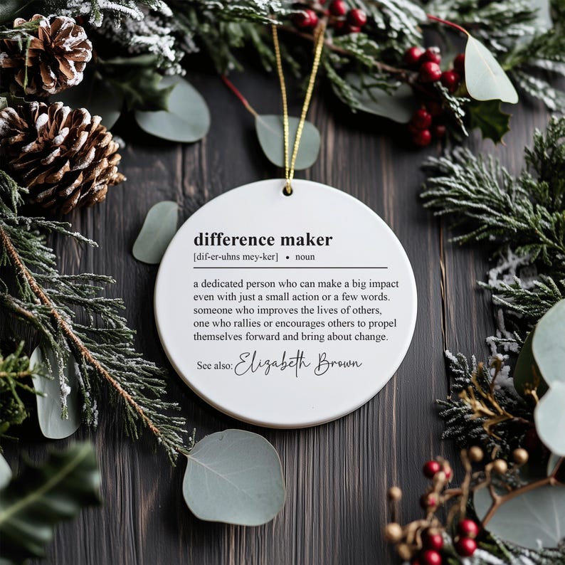 May include: White round Christmas bauble with black text defining "difference maker" as a dedicated person who can make a big impact. The bauble also includes the text "See also: Elizabeth Brown".