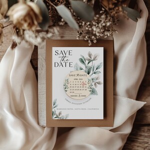 Puede incluir: Tarjeta de guardar la fecha con un dise&ntilde;o floral de acuarela. La tarjeta presenta un calendario con la fecha marcada en rojo. El texto en la tarjeta dice "Save the Date", "Abril 2024", "Amanda & David", "Invitaci&oacute;n formal a seguir", y "Marigold Hotel Santa Rosa, California".